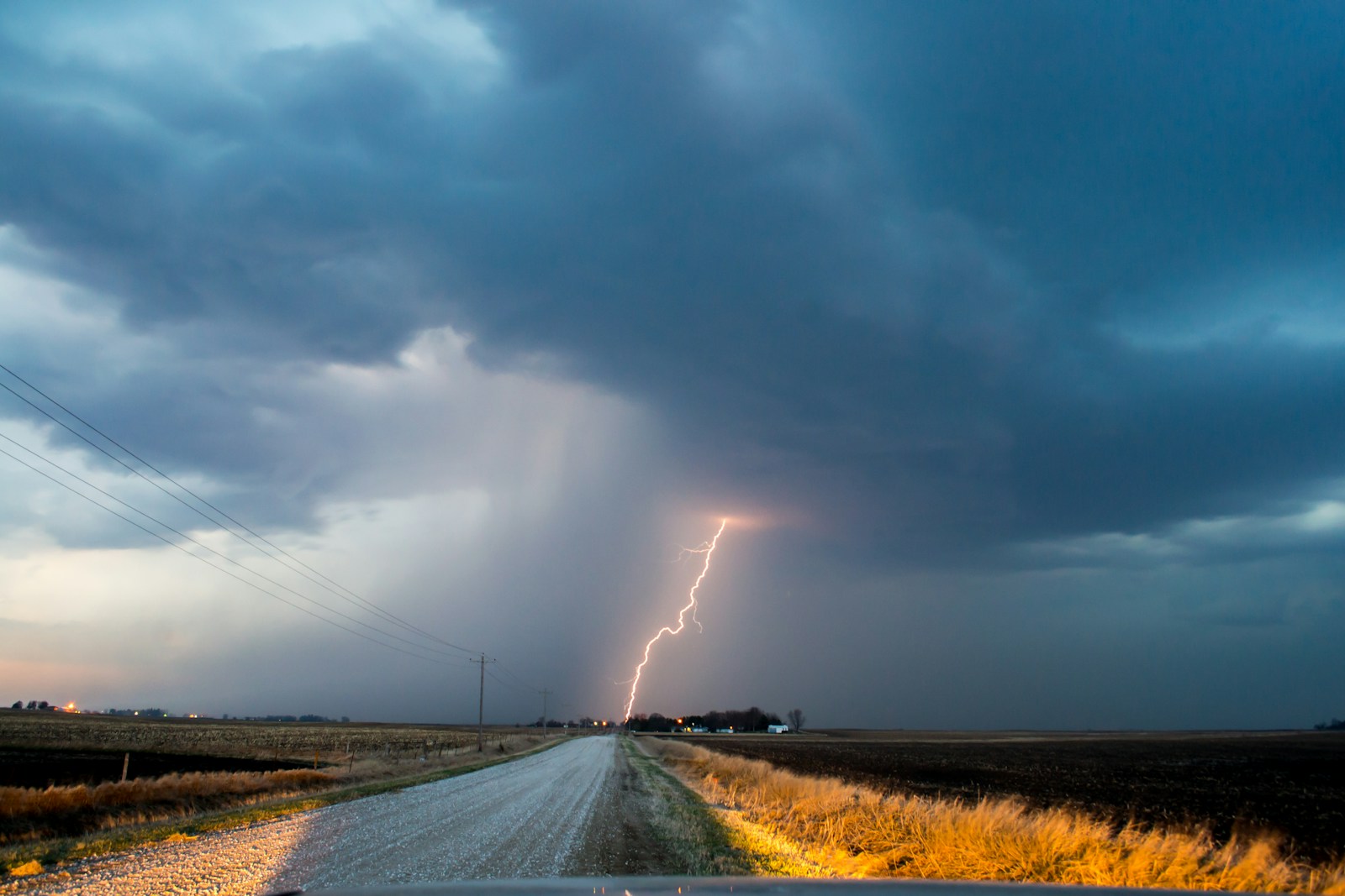 empty road with heavy stormclouds and a bolt of lightning hitting the ground ahead