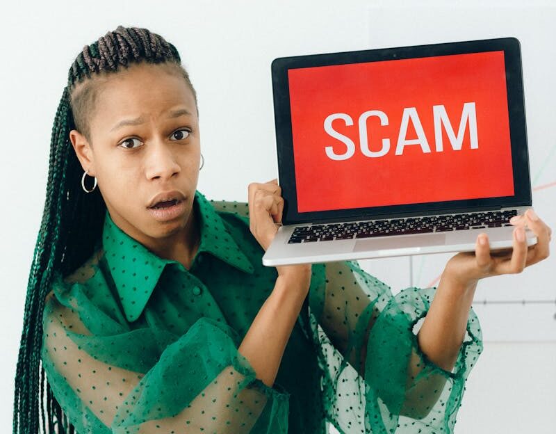 A shocked woman holding a laptop displaying a scam alert in a bright room.