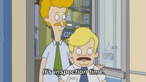 Two cartoon characters, in shirts and ties. The shorter one pulls on a rubber glove, and the caption says "it's inspection time"